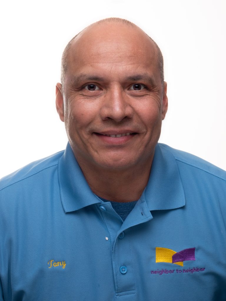 N2N-Tony smiling brown-skinned man with shaved head in pale blue Neighbor to Neighbor branded polo